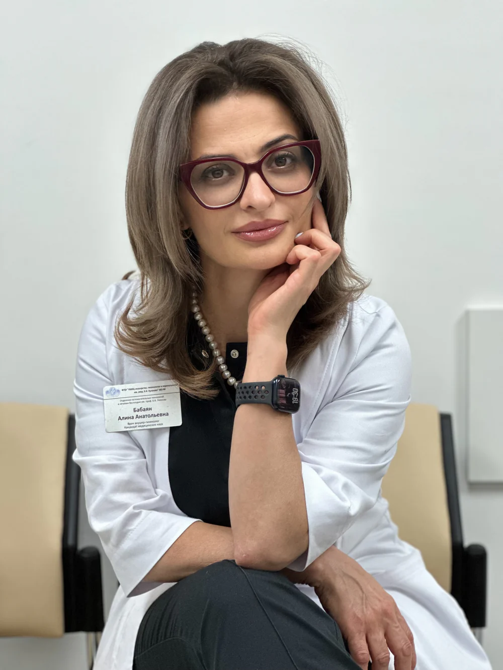 Алина Бабаян в белом халате сидит, опираясь рукой на щёку